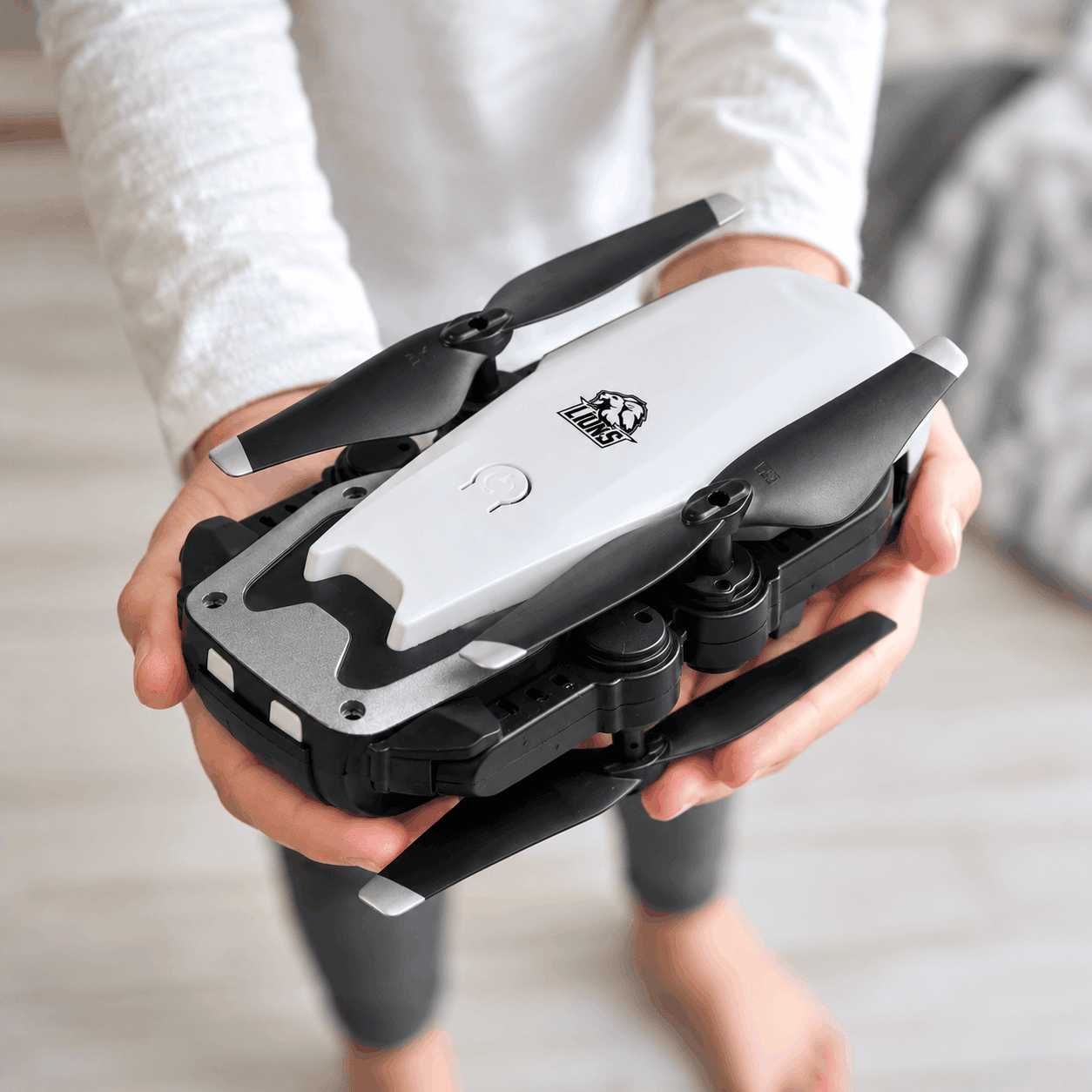 White and black BirdEye remote control camera drone with a custom black logo, featuring foldable propeller arms and a compact design, held in both hands indoors.