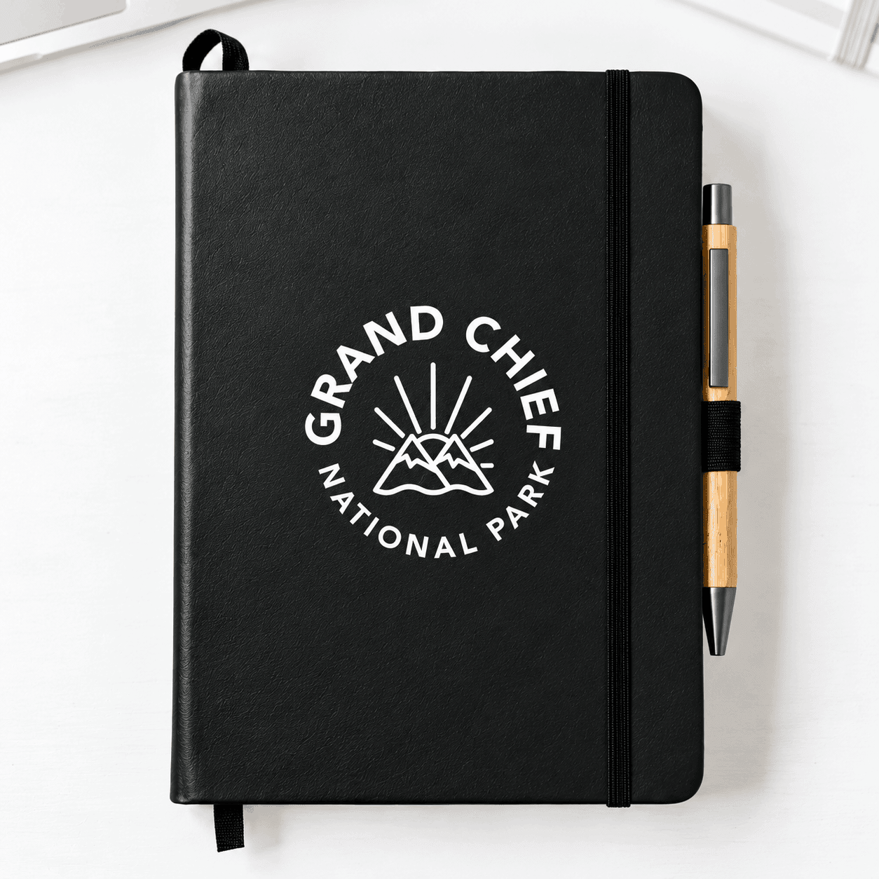 Black cactus leather-bound journal featuring a white Grand Chief National Park logo, elastic closure, ribbon bookmark, and matching pen on a white surface.