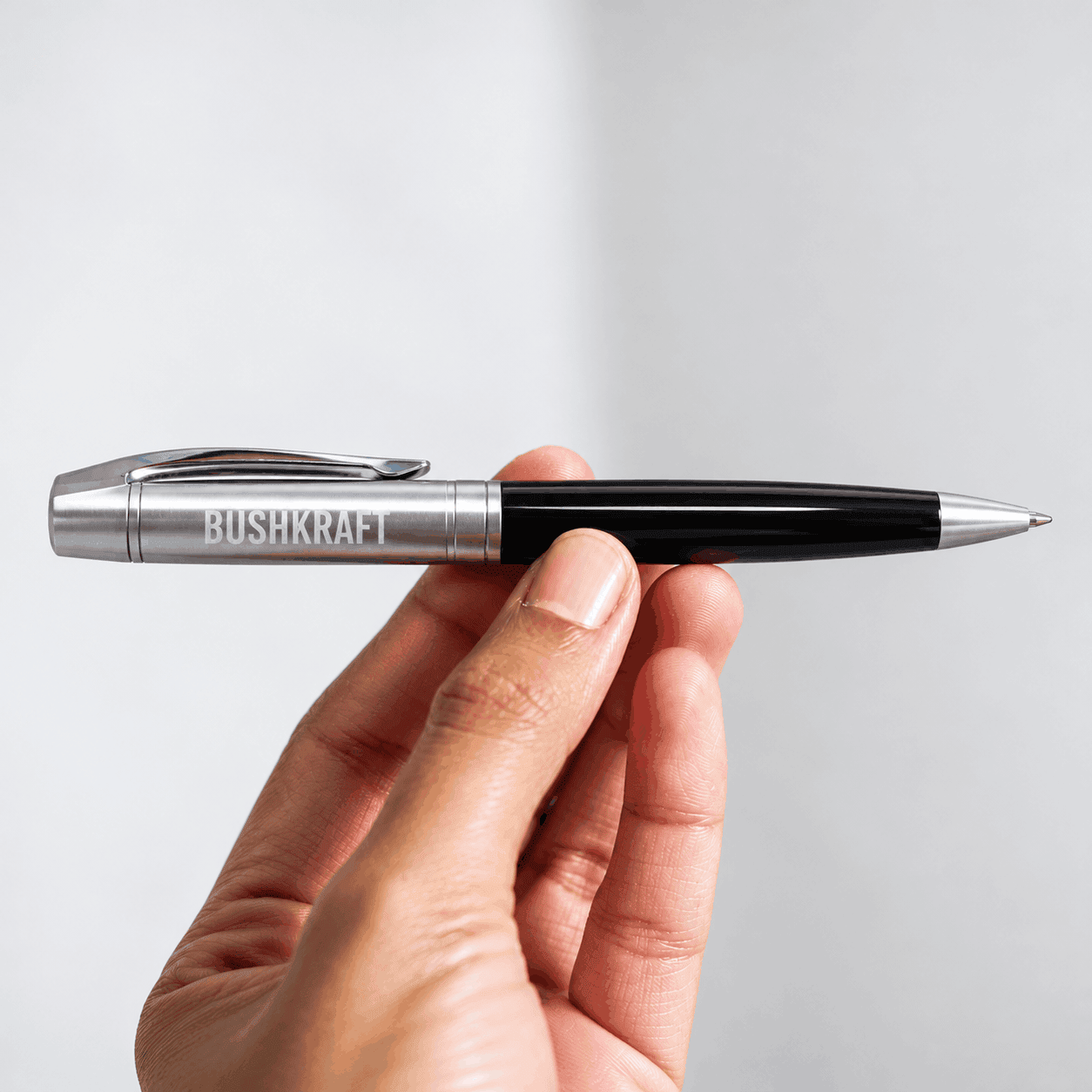 Glossy black Sheaffer 300 ballpoint pen with polished chrome accents and a custom BUSHKRAFT engraving, held against a clean light gray background.