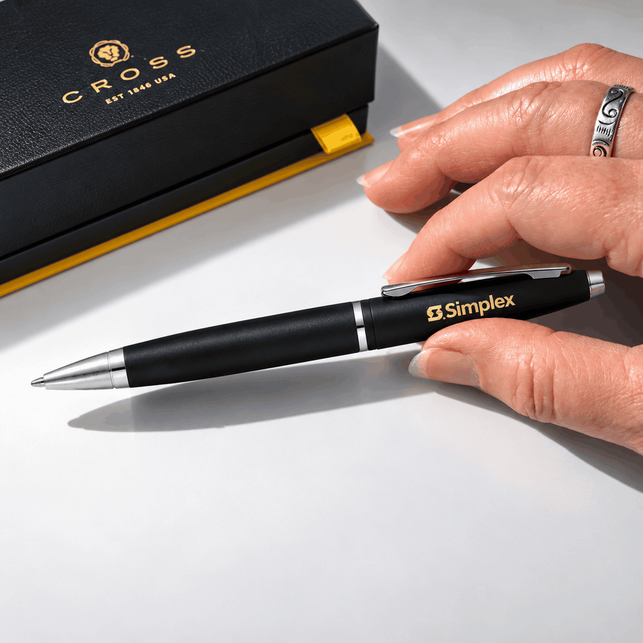 Matte black Cross Calais ballpoint pen with silver accents and a custom gold Simplex logo, displayed beside a black Cross gift box on a white surface.
